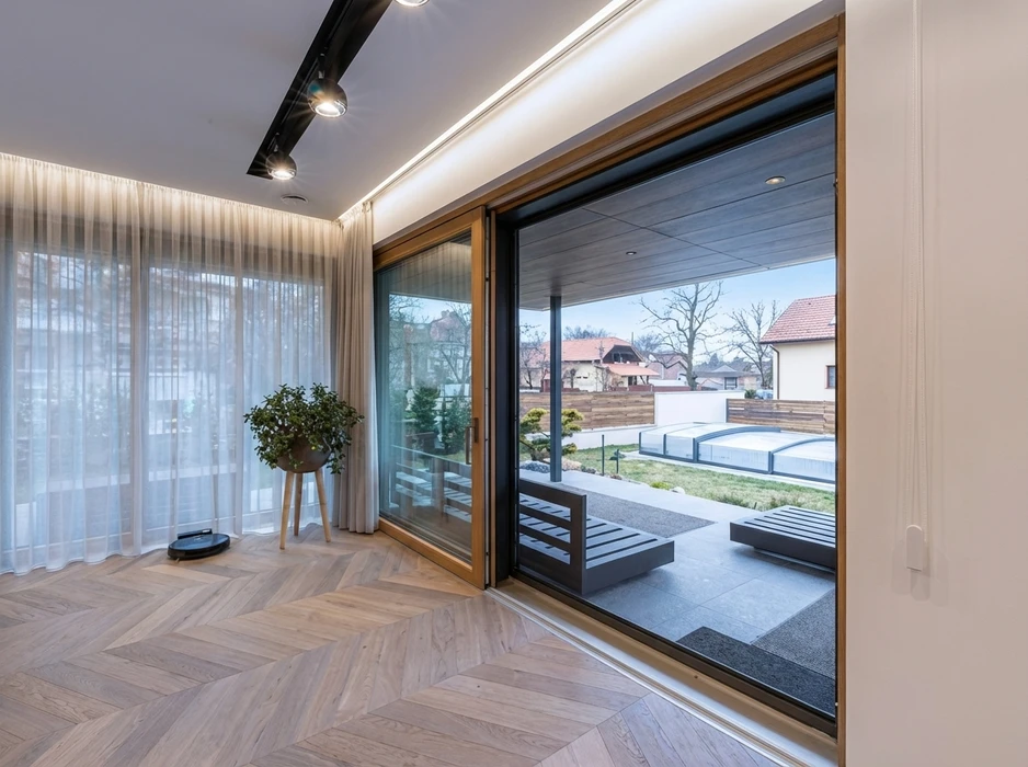 Intérieur moderne avec baie vitrée coulissante à cadre bois et aluminium anthracite ouvrant sur une terrasse couverte avec pool-house