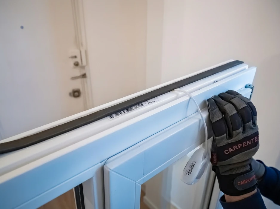 Technicien ganté (gants Carpenter) manipulant un cadre de fenêtre PVC blanc lors d'une installation intérieure