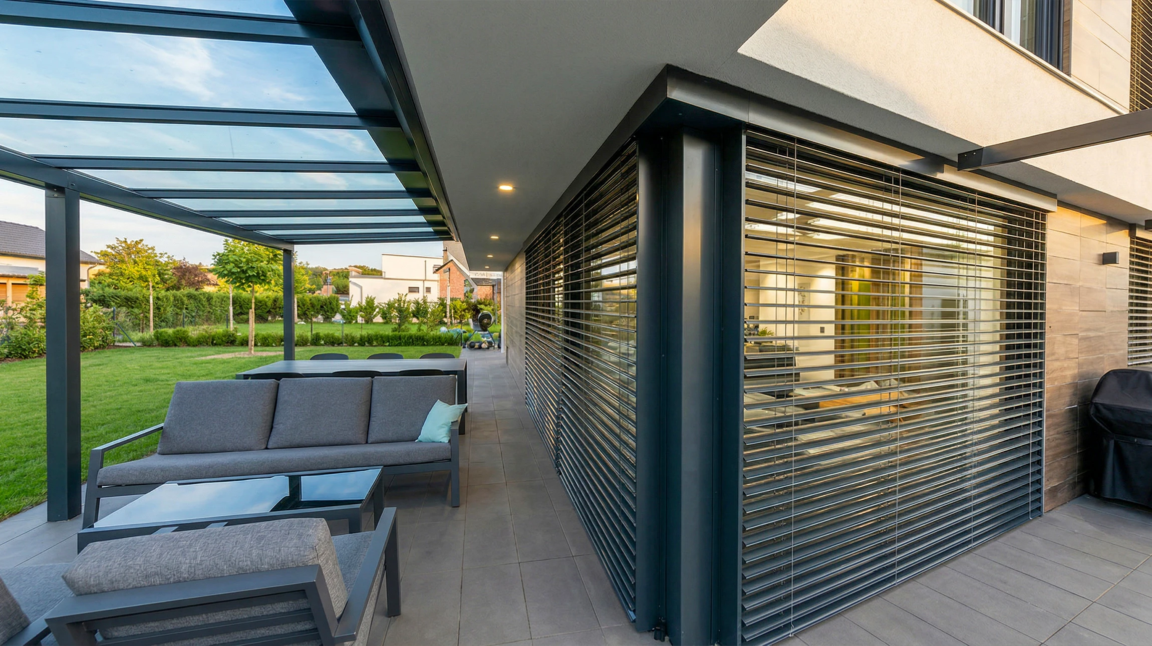 Terrasse moderne avec pergola bioclimatique à lames orientables, mobilier de jardin en résine tressée disposé sous l'abri